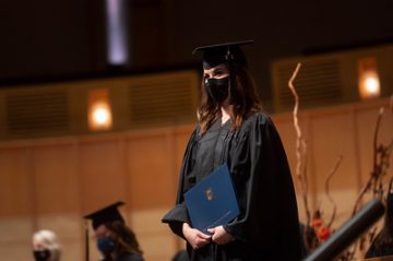 Student in cap and gown, holding a UBC diploma.